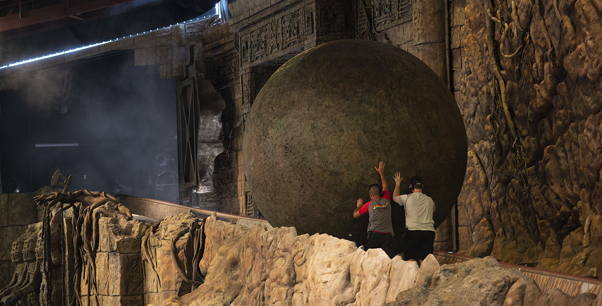 Two Disney Cast Members push a boulder up an Indiana Jones Adventure ramp.