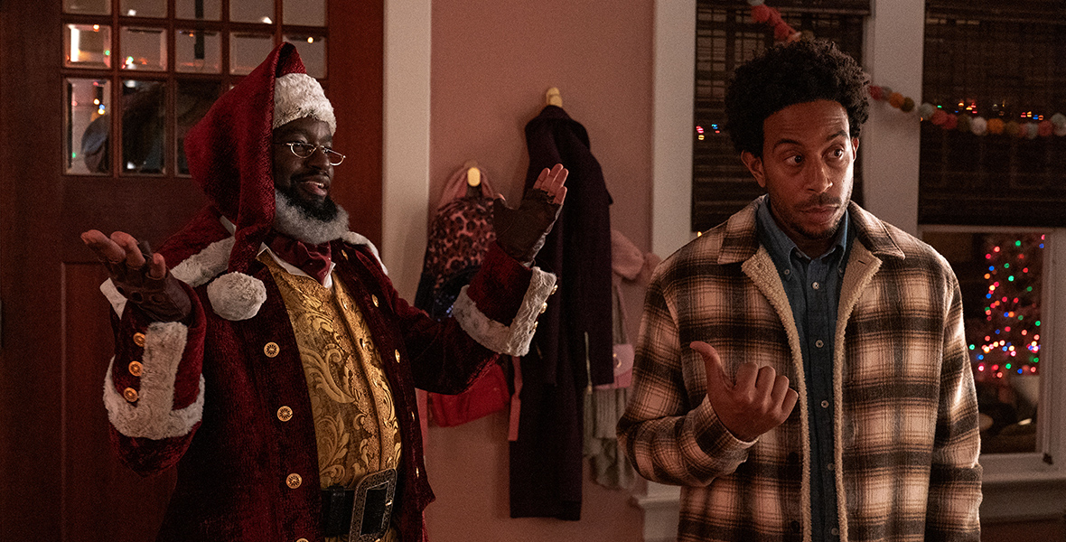 Nick, played by Lil Rel Howery, and Eddie, played by Chris Bridges aka Ludacris stand next to each other. Nick is in a Santa suit and has his arms up while smiling. Eddie has a blank look on his face as he looks away from Nick while pointing at him.