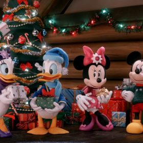 Standing in a log cabin are five stop-motion Disney characters, all dressed in Christmas attire and, except for Mickey Mouse, holding a wrapped Christmas present. Pictured from left to right are Goofy, Daisy Duck, Donald Duck, Minnie Mouse, Mickey Mouse, and Pluto. Behind them, more wrapped gifts are sitting on the floor beneath a decorated Christmas tree and a log wall decorated with a lighted garland and a lighted wreath.