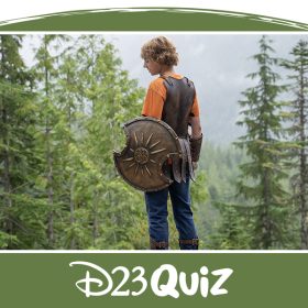 Percy Jackson stands with his back to the viewer, slightly looking over his left shoulder. He is holding a bronze shield in his left hand. In the distance is a thick forest of pine trees