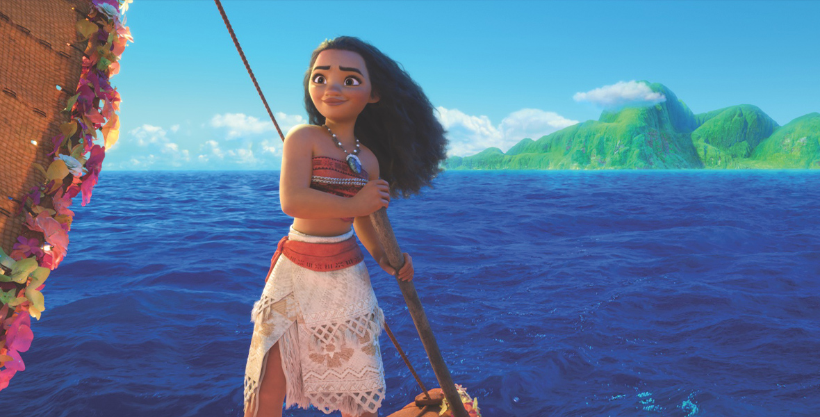 In an image from Walt Disney Animation Studios’ Moana, Moana (voiced by Auli’i Cravalho) is on the back of her vessel, steering by holding an oar; there is an island in the distance behind her, and her hair is swept back somewhat by the wind.