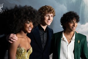 In an image from the world premiere for Disney+’s Percy Jackson and the Olympians, from left to right, Leah Sava Jeffries (Annabeth Chase), Walker Scobell (Percy Jackson), and Aryan Simhadri (Grover Underwood) are seen smiling for cameras on the red carpet.