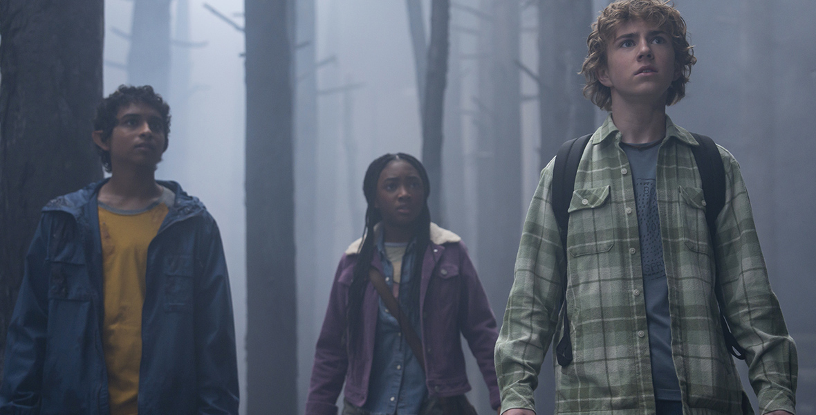 The three leads from Percy Jackson and the Olympians—Percy Jackson, played by Walker Scobell; Annabeth Chase, played by Leah Jeffries; and Grover Underwood, played by Aryan Simhadri—stand in a foggy forest and stare ahead.