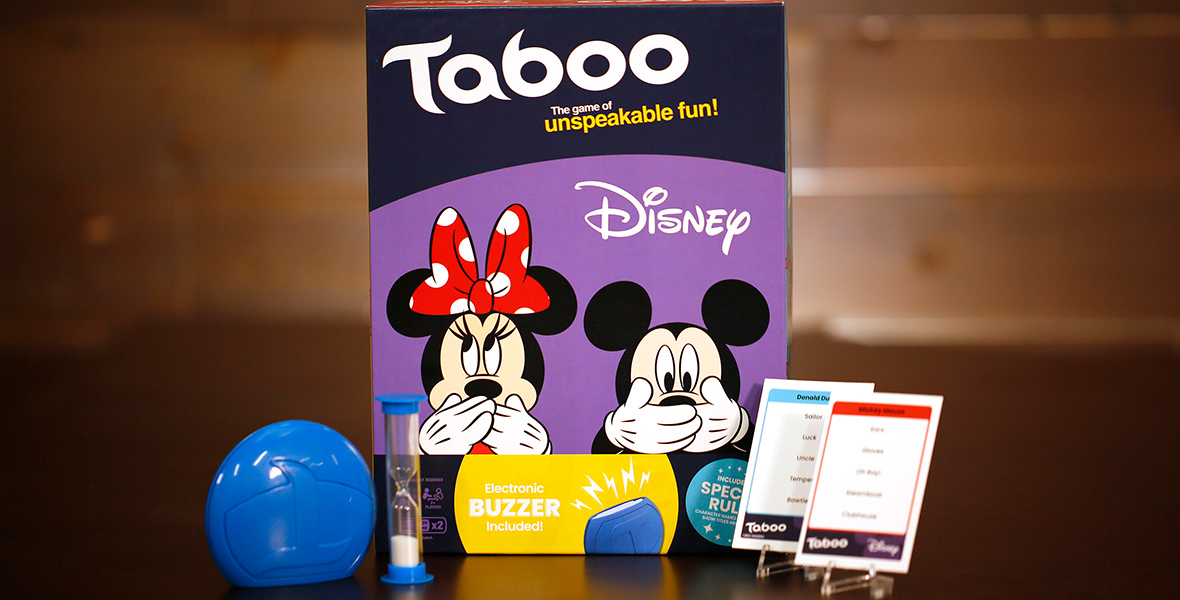 The box for TABOO®: Disney Edition sits against a wooden backdrop. The box is purple and features Minnie and Mickey covering their mouths with both hands. In front of the box is a blue buzzer, an hourglass, and two cards from the game.