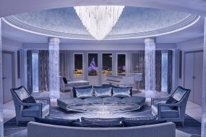 The Frozen Signature Suite has a chandelier hanging above a round table. The room has a silvery blue color scheme. Sleeping Beauty Castle is seen through the window.