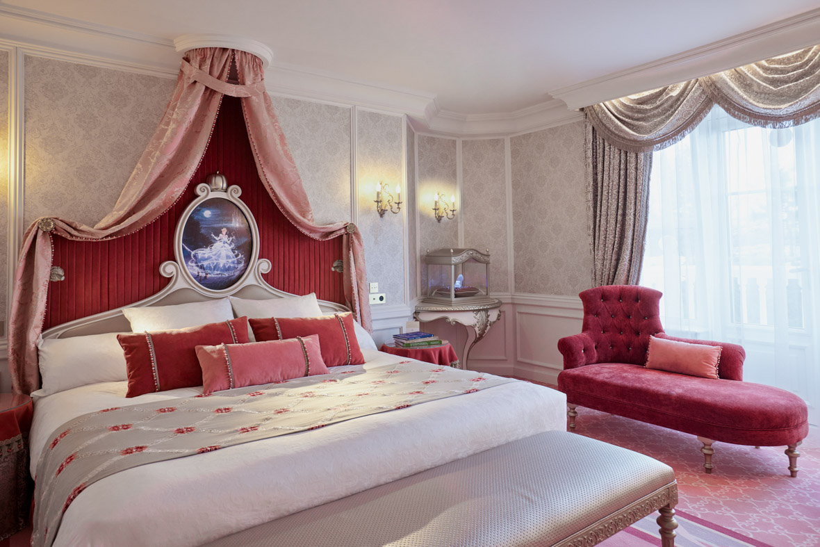 The Cinderella Signature Suite features bed adorned with pillows and a neatly folded blanket. A canopy above the headboard depicts a scene from the film Cinderella.