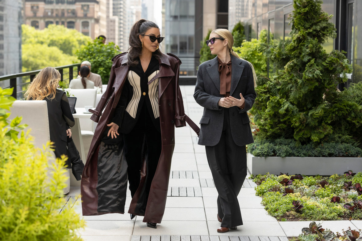 In a scene from American Horror Story: Delicate, Siobhan Corbyn, played by Kim Kardashian, walks beside Anna Victoria Alcott, played by Emma Roberts, on a rooftop deck.