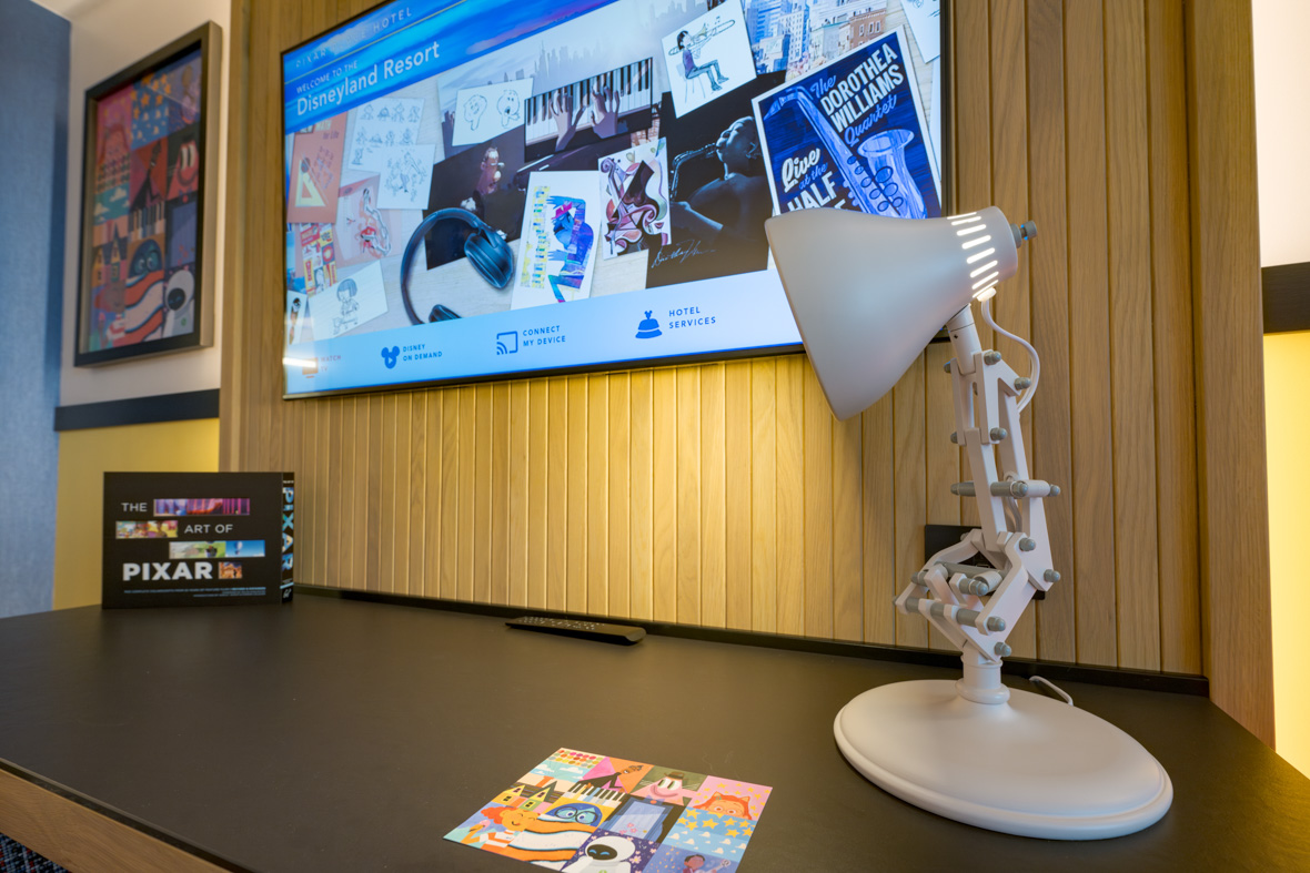 The desk in a guest room at Pixar Place Hotel sports a replica of the Pixar lamp, serving as a working desk lamp. Above the desktop is a flatscreen TV.