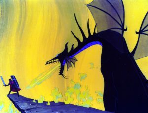 Maleficent in dragon form has cornered Prince Philip at the edge of a cliff. The dragon is breathing fire toward the prince, who is defending himself with a shield and sword. The background of the photo is of large flames. 