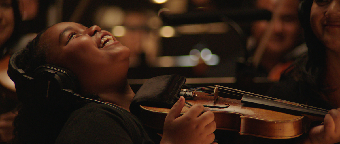 In a scene from Searchlight Pictures' The Last Repair Shop, young aspiring musician Porche Brinker plays the violin. She laughs so hard she's thrown her head back.