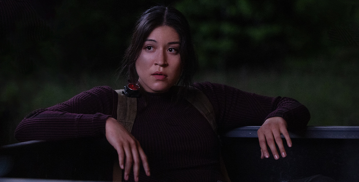 In an image from Marvel Studios’ Echo, Maya Lopez (Alaqua Cox) is leaning back on what appears to be the bed of a truck, wearing dark clothing and looking at something off camera to the left.