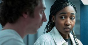 In a scene from The Bear, a seemingly concerned Sydney Adamu, played by Ayo Edebiri, looks at an out-of-focus Carmen "Carmy" Berzatto, played by Jeremy Allen White.