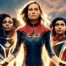 In a promotional poster for Marvel Studios' The Marvels, Monica Rambeau, played by Teyonah Parris, Carol Danvers, played by Brie Larson, and Kamala Khan, played by Iman Vellani, strike classic Super Hero poses. They respectively emit white, gold, and purple light.