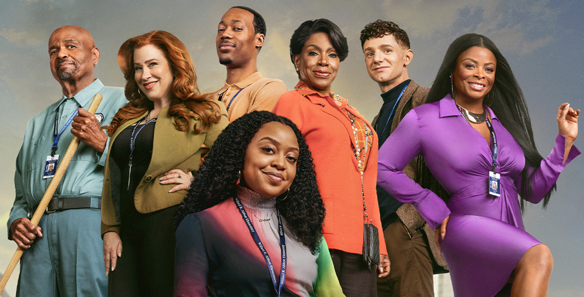 The Abbott Elementary cast—William Stanford Davis, Lisa Ann Walter, Tyler James Williams, Quinta Brunson, Sheryl Lee Ralph, Chris Perfetti, and Janelle James—smiles for a group photo. Brunson is seated in the center, while everyone else is standing.