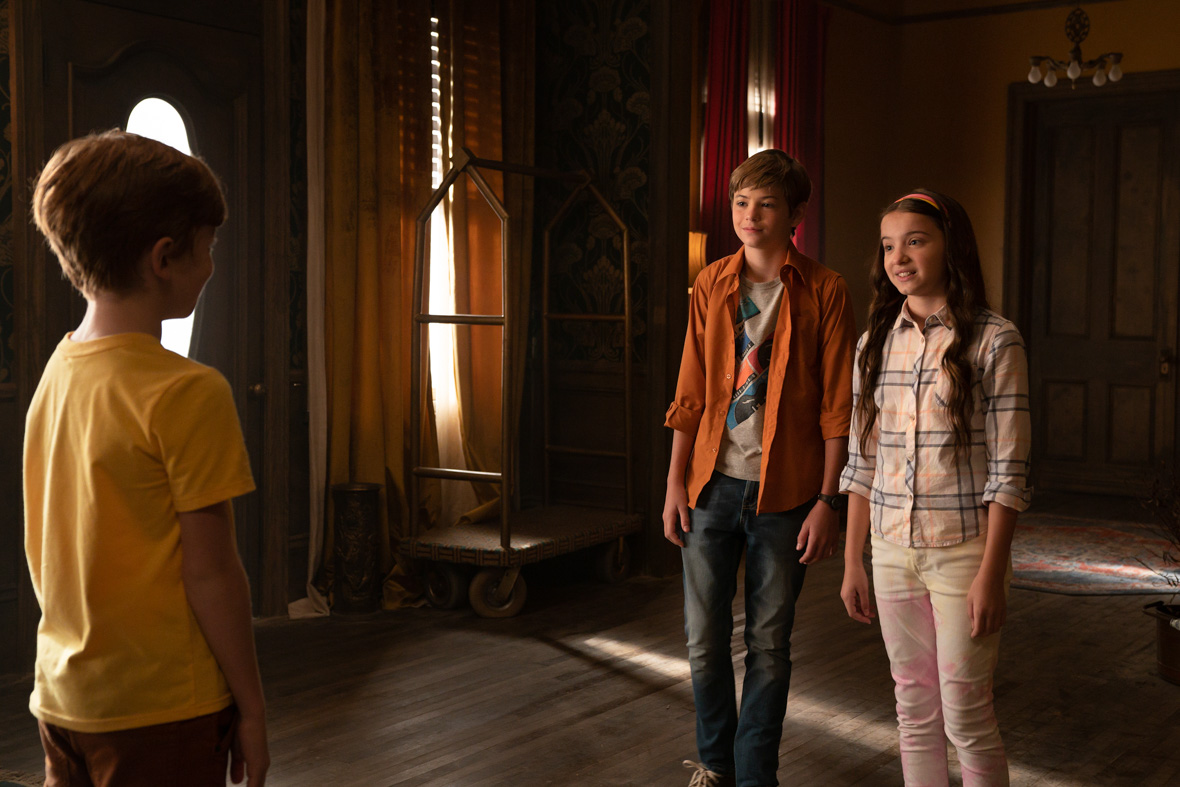 Inside a home with wooden floors, Wyatt, played by Landon Gordon, in a yellow T-shirt, faces Griffin, played by Preston Oliver, wearing an orange shirt, a gray t-shirt, and jeans. Zoey, played by Madeleine McGraw, sporting a checked shirt and tie-dye white jeans, stands next to Griffin.