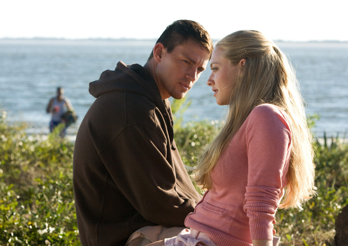 John (left), played by Channing Tatum, and Savannah (right), played by Amanda Seyfried, are sitting on a bench before the beach. John is wearing a brown hoodie and is looking at Savannah, while she is looking ahead and is wearing a pink cardigan.