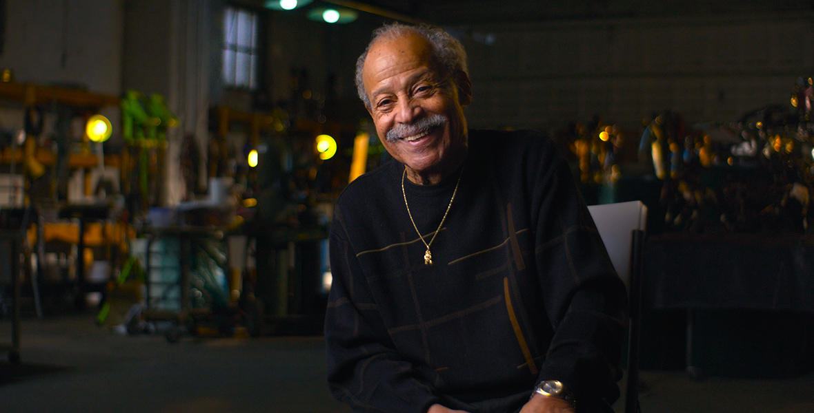 Former test pilot Ed Dwight smiling during an interview.  He is wearing a black crewneck, a gold necklace, and black pants.