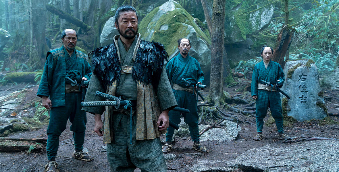 In a scene from FX's Shōgun, Kashigi Yabushige, played by Tadanobu Asano, stands in the foreground, wearing a jade green outfit. Three men stand behind him in a lush forest.