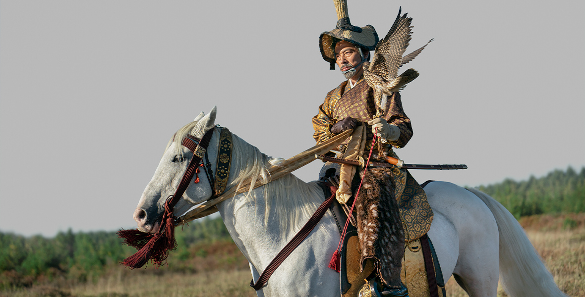 In a scene from FX's Shōgun, the powerful bushō Yoshii Toranaga, played by Hiroyuki Sanada, rides a white horse. His ornate outfit features a large bird on his shoulder.