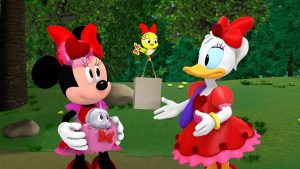 Minnie (left) is wearing a pink and red dress and a red bow adorned with a red heart. She is holding a grey bunny in a pink pouch placed around her waist. Daisy Duck (right) is wearing a red voluminous dress and a red bow adorned with a red rose. A yellow bird flying between Minnie and Daisy is delivering a grey bag to Daisy.