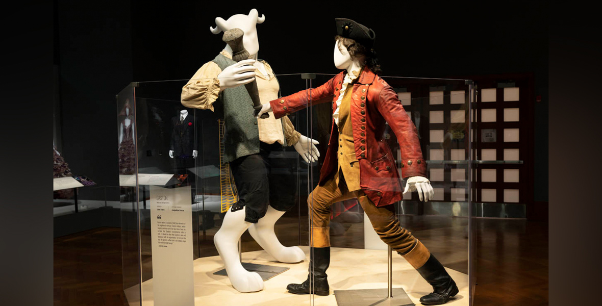 Costumes designed by Jacqueline Durran for the Beast (played by Dan Stevens) and Gaston (played by Luke Evans) in Beauty and the Beast (2017), are displayed in Heroes & Villains: The Art of the Disney Costume at the Henry Ford Museum of American Innovation in 2022. Modeled by faceless mannequins, the costumes are Beast’s cream-colored shirt, green vest, and black shorts, left, and Gaston’s red military-style frock coat, right, with burnt orange vest, brown pants, and black boots.