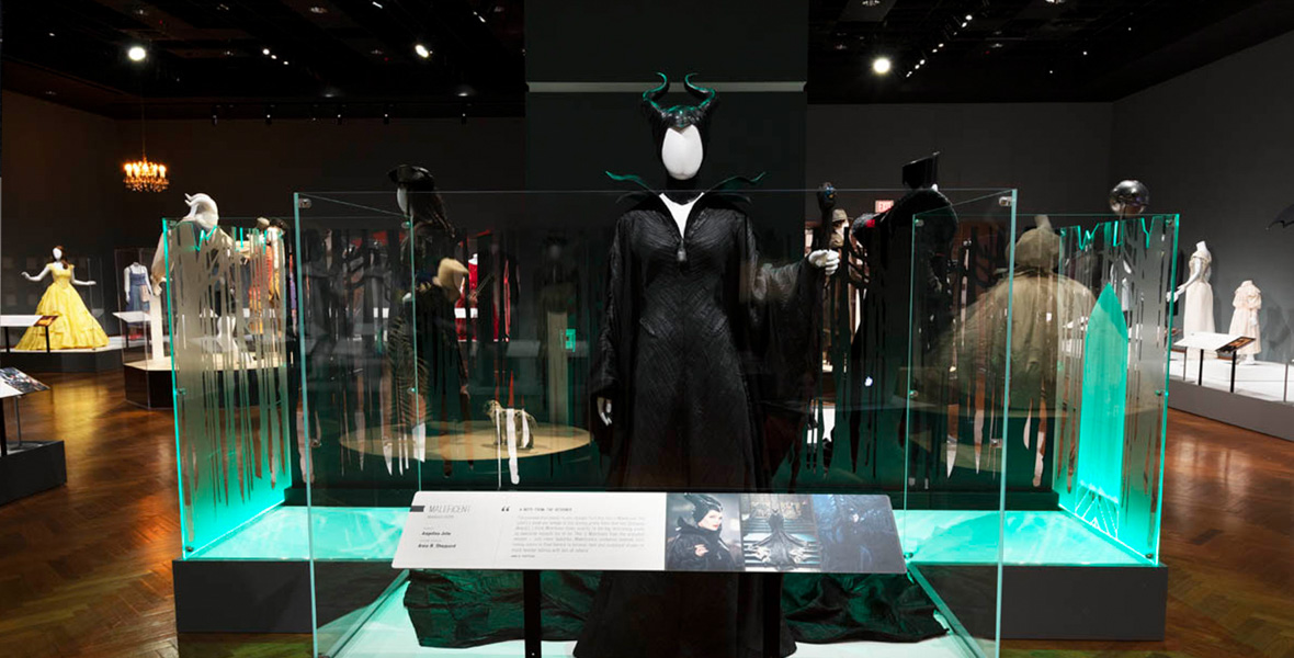 A costume designed by Anna B. Sheppard for Maleficent (played by Angelina Jolie) in Maleficent (2014), is displayed in Heroes & Villains: The Art of the Disney Costume at the Henry Ford Museum of American Innovation® in 2022. Surrounding the Maleficent costume are many other displays of outfits and related items in a large gallery space.