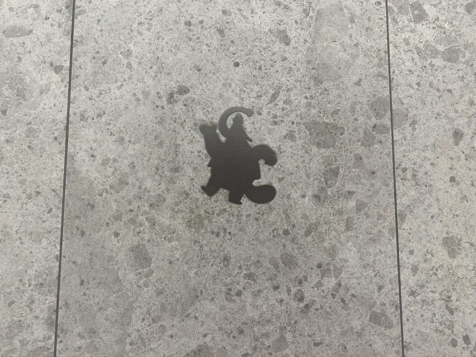 A metal, silver medallion in the shape of Bing Bong from Inside Out is inlaid in the gray floor of the Pixar Place Hotel.