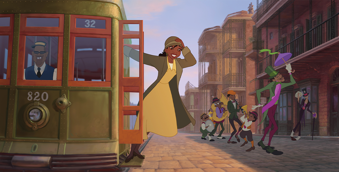 Still from The Princess and the Frog film, featuring Tiana leaning out from a moving Trolley looking out into the French quarter of New Orleans. The Villainous Dr. Facilier is present in the shadows, fanning out a deck of Tarot cards. Next to the Trolley is a colorful “second line” parade processional of Jazz musicians.
