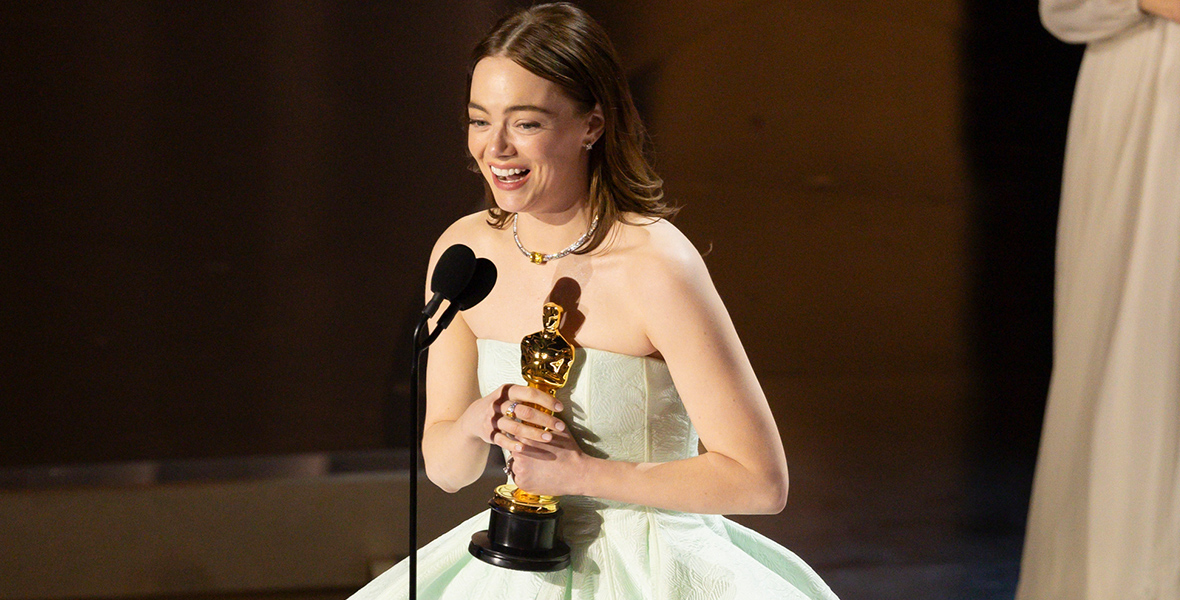 Emma Stone wears a mint green dress and holds a gold Oscar statue.