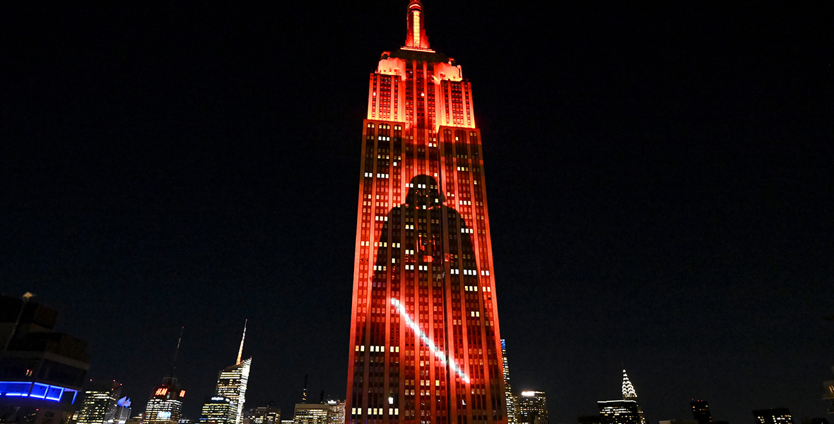 The Empire State Building is illuminated with red lights, outlining an image of Darth Vader, against the backdrop of New York City’s skyline at night.