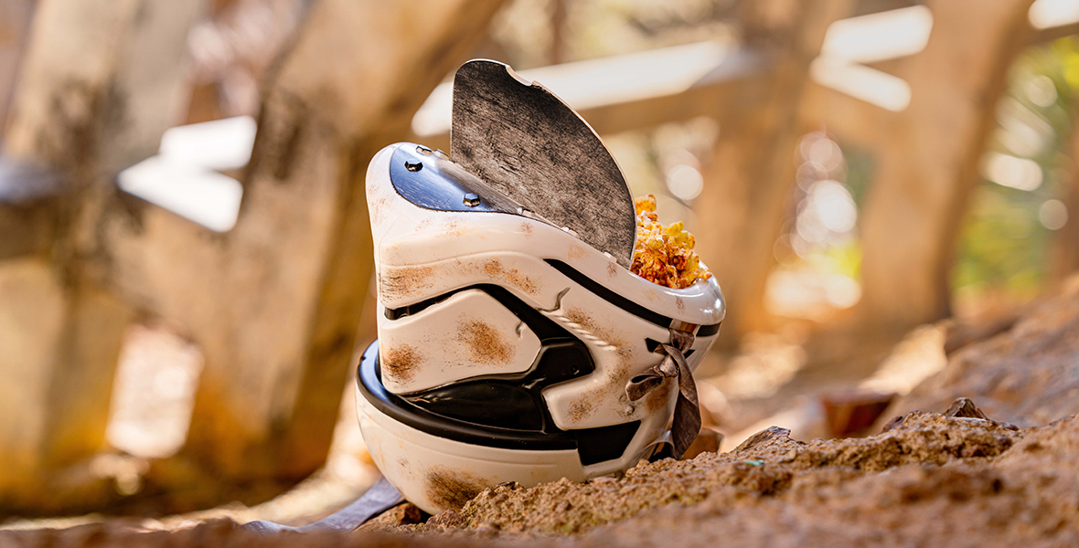 A collectible Salvaged Stormtrooper Helmet Bucket served with popcorn is pictured on muddy terrain. 