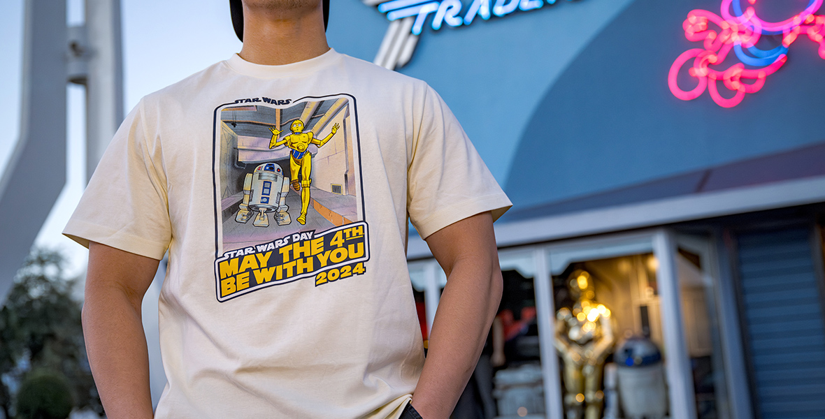 A boy standing outside the “THE STAR TRADER” store is wearing a white T-Shirt that reads “MAY THE 4TH BE WITH YOU 2024.” 