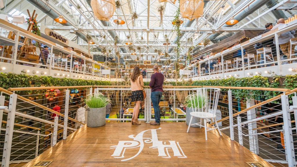 Couple standing inside the main building of the Anaheim Packing House looking over into the large spacious atrium of the food hall.