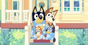 In a scene from the series Bluey, Chilli, Bandit, Bluey, and Bingo, a family of Australian Cattle dogs, are sitting on the porch of their home. Chilli, the family’s mother, and Bingo, the family’s youngest, are Red Heelers, and Bandit, the family’s father, and Bluey, the family’s first child, are Blue Heelers. All members are looking calmly at the camera, but Bingo is frightened.