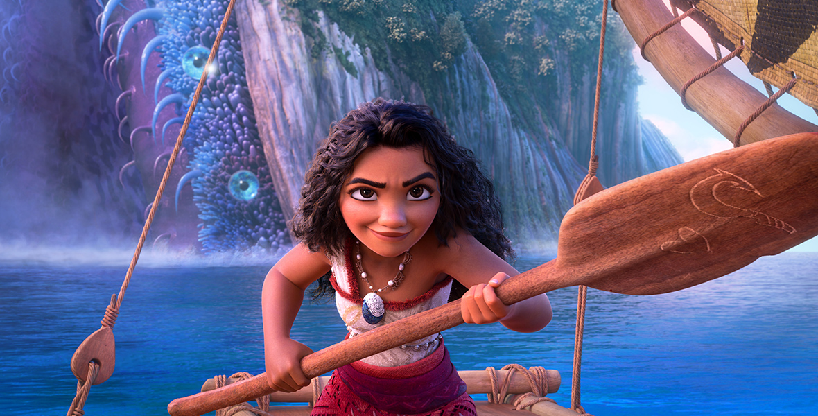 Moana, standing on her boat, looks ahead at the camera with a determined expression, holding her oar up across her chest. Behind her is lush scenery of an island, that seems to have both plant life and strange tentacles and growths growing on it.