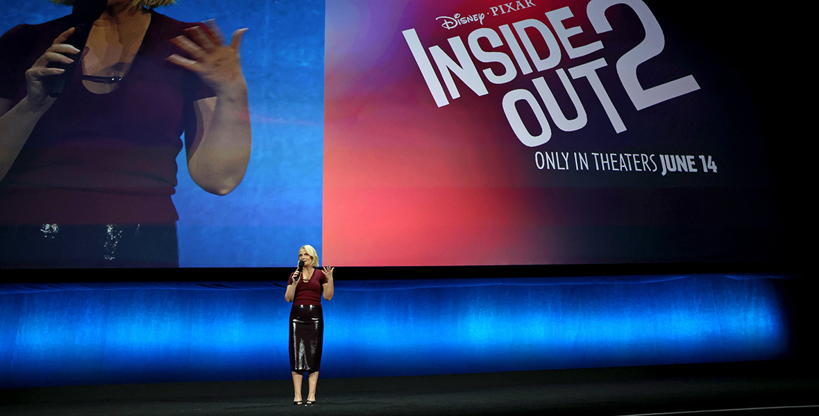 Amy Poehler speaks onstage during the Walt Disney Studios presentation at Cinemacon. On screen behind her is a split image of live video of herself speaking and the logo for the film Inside Out 2.