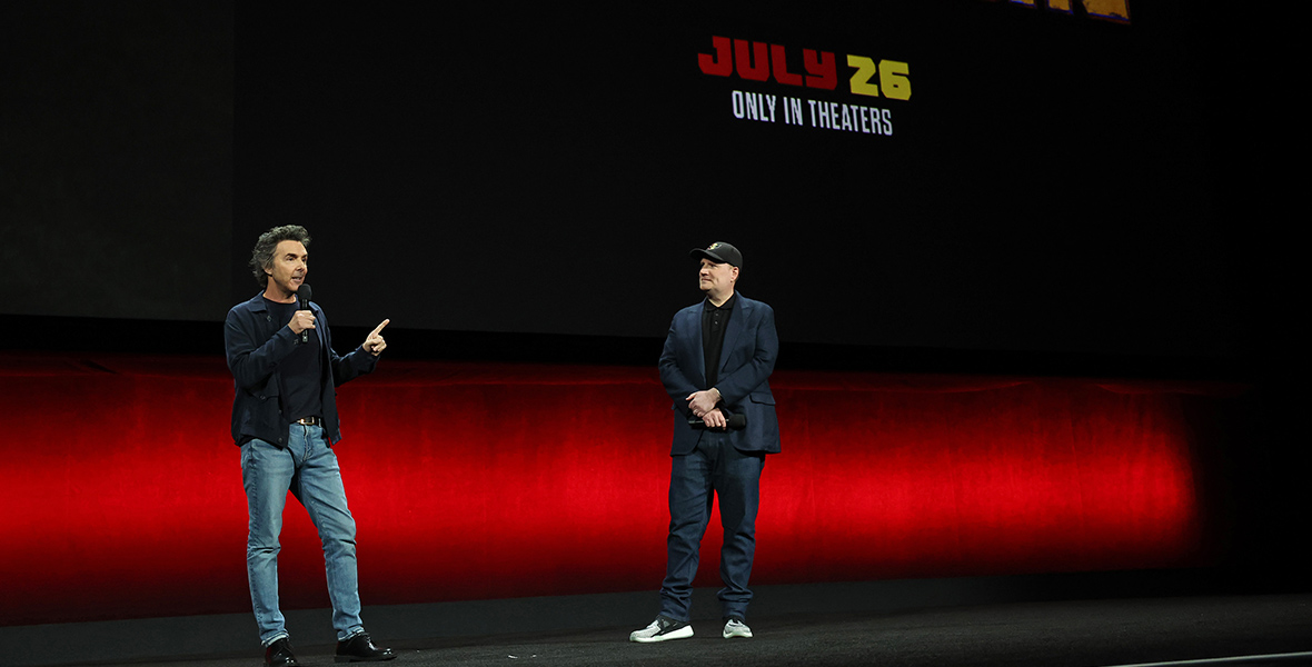 Deadpool & Wolverine director Shawn Levy and Kevin Feige, President, Marvel Studios speak onstage during the Walt Disney Studios presentation at Cinemacon. Behind them onscreen is the logo for the film, with only the yellow text “& Wolverine” visible in the picture. Below the logo is the text “July 25, Only in Theaters”