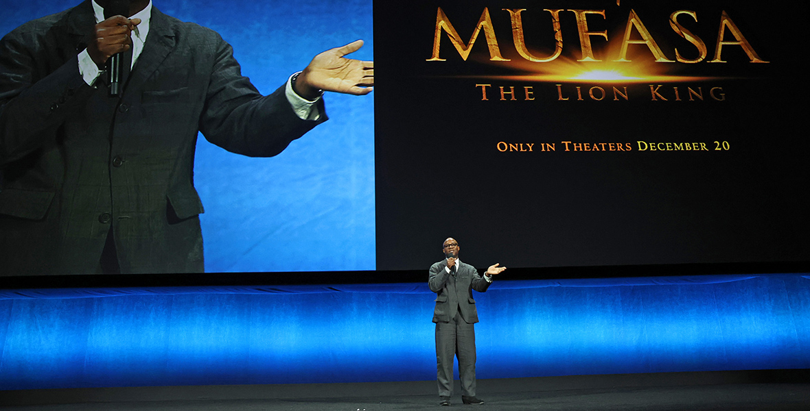Mufasa: The Lion King director Barry Jenkins speaks onstage during the Walt Disney Studios presentation at Cinemacon. Behind him is a split screen of Jenkins speaking and the film’s logo.