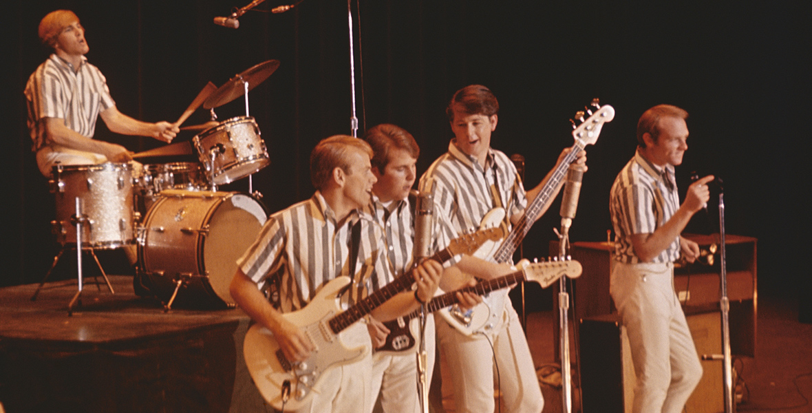 In a scene from the upcoming documentary The Beach Boys, the band is performing onstage circa 1964 in California. Dennis Wilson is seen playing the drums at the back, positioned higher than the rest of the band. At center stage are Al Jardine, Carl Wilson, Brian Wilson, and Mike Love. They are all singing, and (with the exception of Love) playing guitars. The band members are dressed in white and grey striped short-sleeve shirts and white pants.