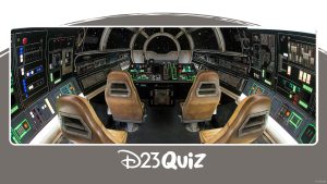 The inside of the Millennium Falcon: Smugglers Run attraction is a faithful recreation of the iconic Star Wars ship, featuring black walls adorned with switches and buttons, and a main view screen surrounded by seats in a semi-circle arrangement. The leather seats are weathered, and neon strips surround some of the buttons.