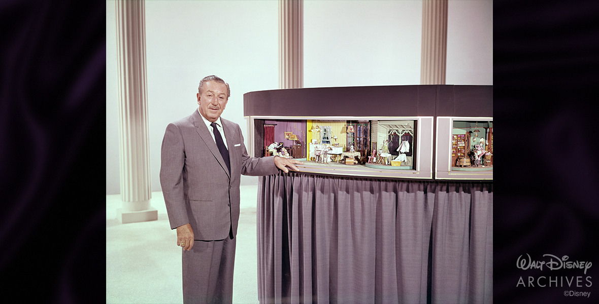 Walt Disney is standing with a model for the Carousel of Progress—1964 New York World’s Fair, 1963, at WED Enterprises Inc. He is wearing a grey suit.