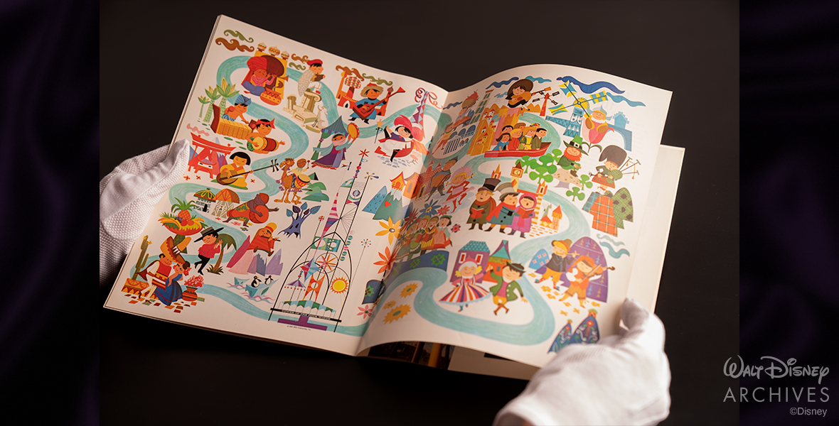 An opened page reveals colorful illustrations from the "it's a small world" souvenir guidebook, dating back to the Fair's heyday.