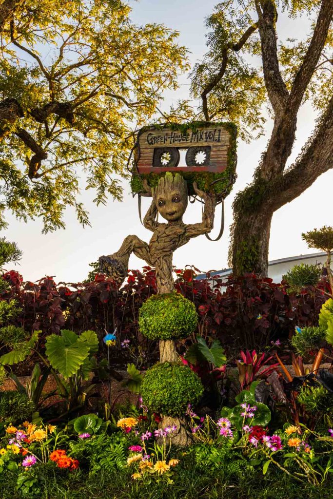 A vertical image of the new Groot topiary at EPCOT, surrounded by plants. 