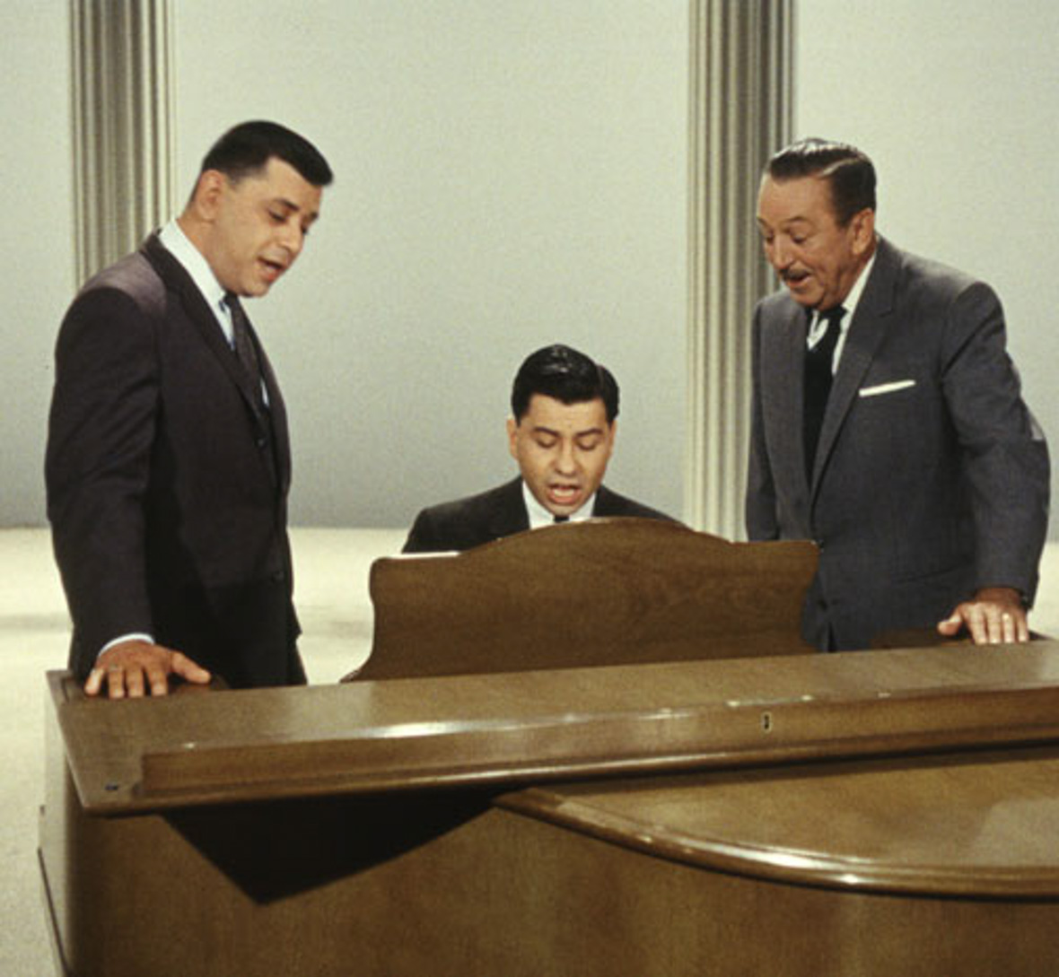 Robert B. Sherman, Richard M. Sherman, and Walt Disney sing at a piano.