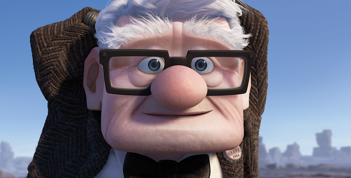 In a scene from the movie Up, Carl (voiced by Edward Asner) is wearing a brown, wool jacket, a black bowtie, a white shirt, and black square glasses. He gazes ahead in amazement. A pin on the left side of his jacket reads “GRAPE SODA.” Behind him, the background reveals a blue sky with large rocks.