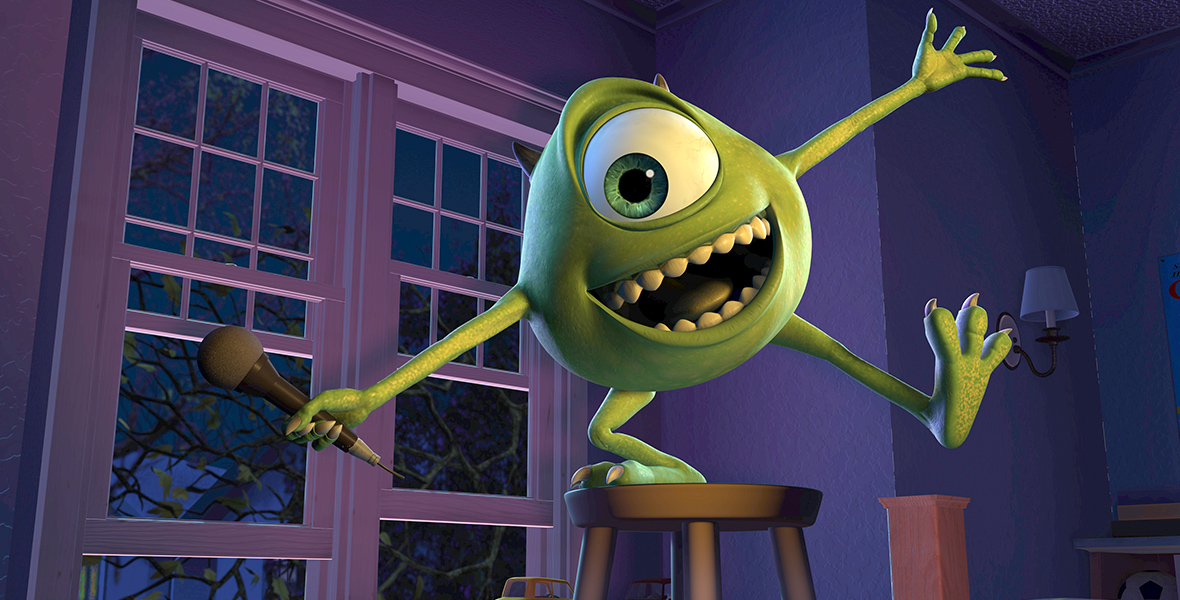 In a scene from Monsters, Inc., Mike Wazowski (voiced by Billy Crystal) is a spherical round lime-skinned monster with a single emerald green, cyclopean eye. Mike is inside a bedroom, holding a microphone in his right hand. Standing on a stool with his right leg, the rest of his limbs stretch out/ The background shows the bedroom walls and windows.
