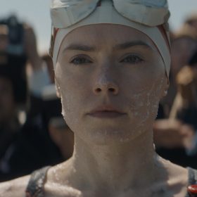 In a scene from Young Woman and the Sea, Trudy Ederle, played by Daisy Ridley, is slathered in porpoise fat and wearing a swim cap and goggles. Photographers surround her.