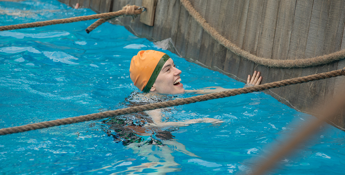 In a scene from Young Woman and the Sea, Trudy Ederle, played by Daisy Ridley, smiles in a swim lane. She is wearing a yellow swim cap.