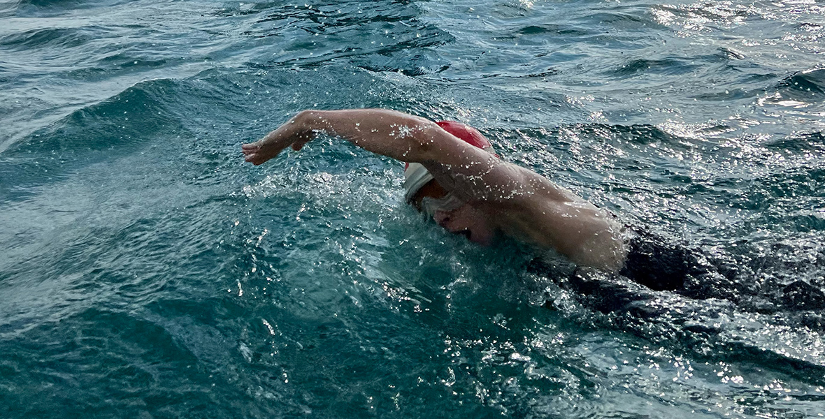 In a scene from Young Woman and the Sea, Trudy Ederle, played by Daisy Ridley, swims in open water as a ship sails nearby.