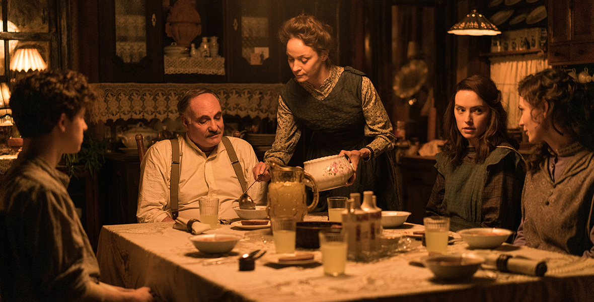 In a scene from Young Woman and the Sea, Henry Ederle Jr., played by Ethan Rouse, Henry Ederle, played by Kim Bodnia, Margaret Ederle, played by Tilda Cobham-Hervey, and Trudy Ederle, played by Daisy Ridley sit around the dinner table as Gertrud Ederle, played by Jeanette Hain, serves dinner.